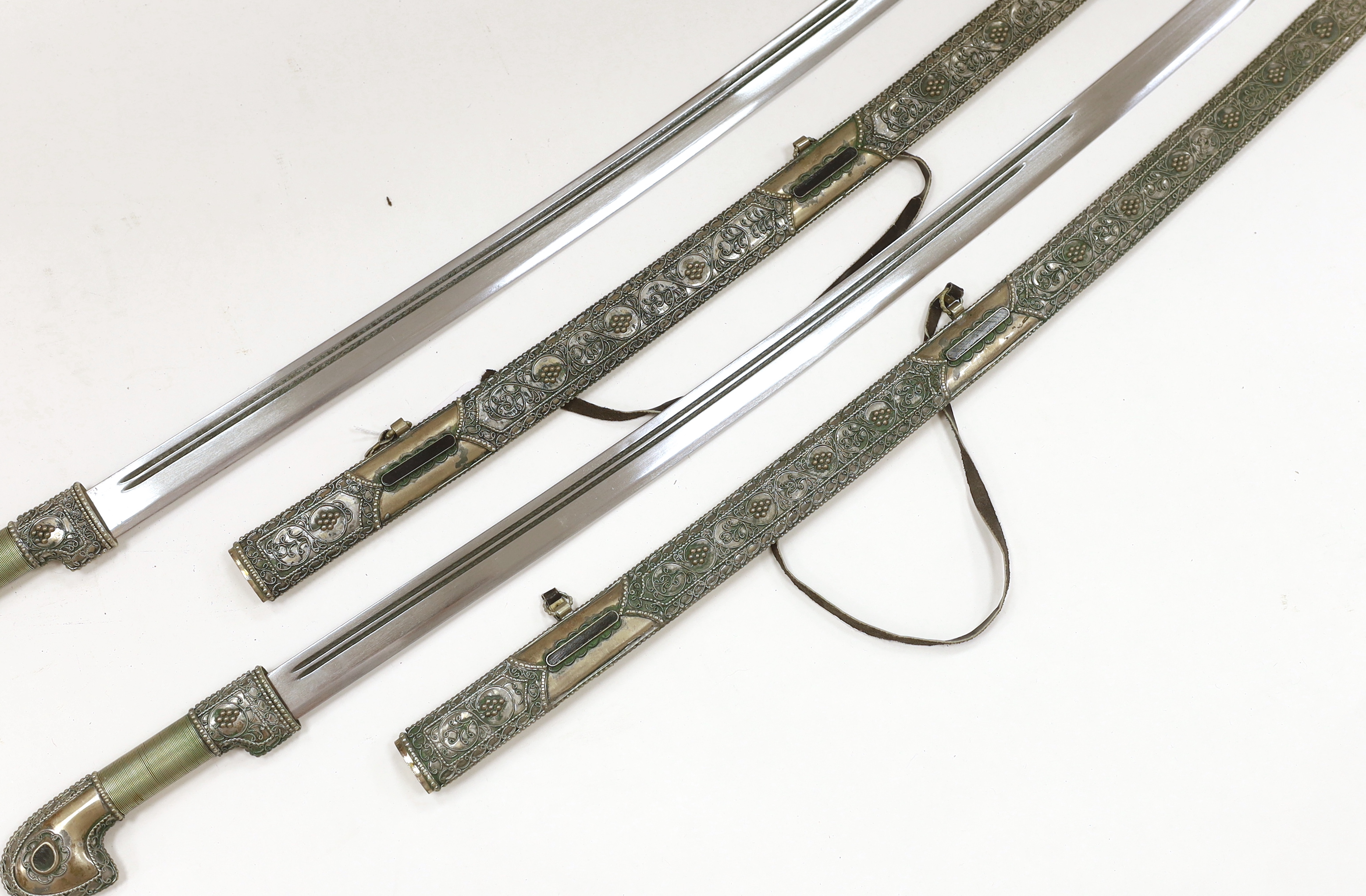 A pair of reproduction Turkish swords with white metal filigree scabbards, blades 80cm